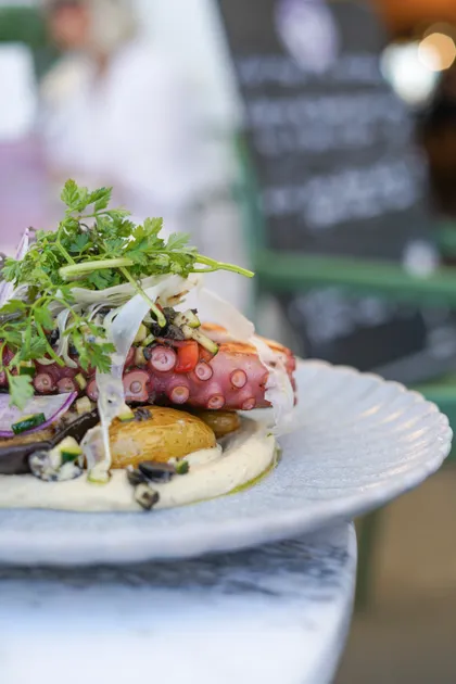 Un plat de poulpe grillé, servi avec des pommes de terre et une sauce verte